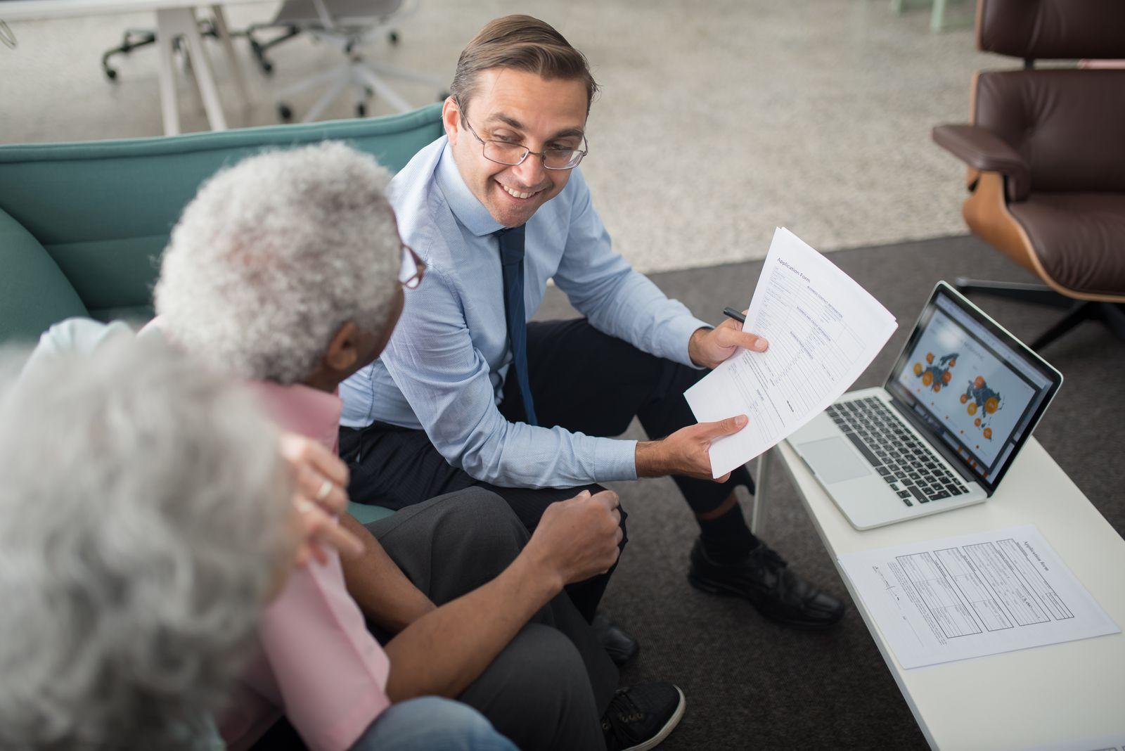 Conseiller présentant un document à des clients lors d'un rendez-vous, ordinateur portable ouvert sur la table