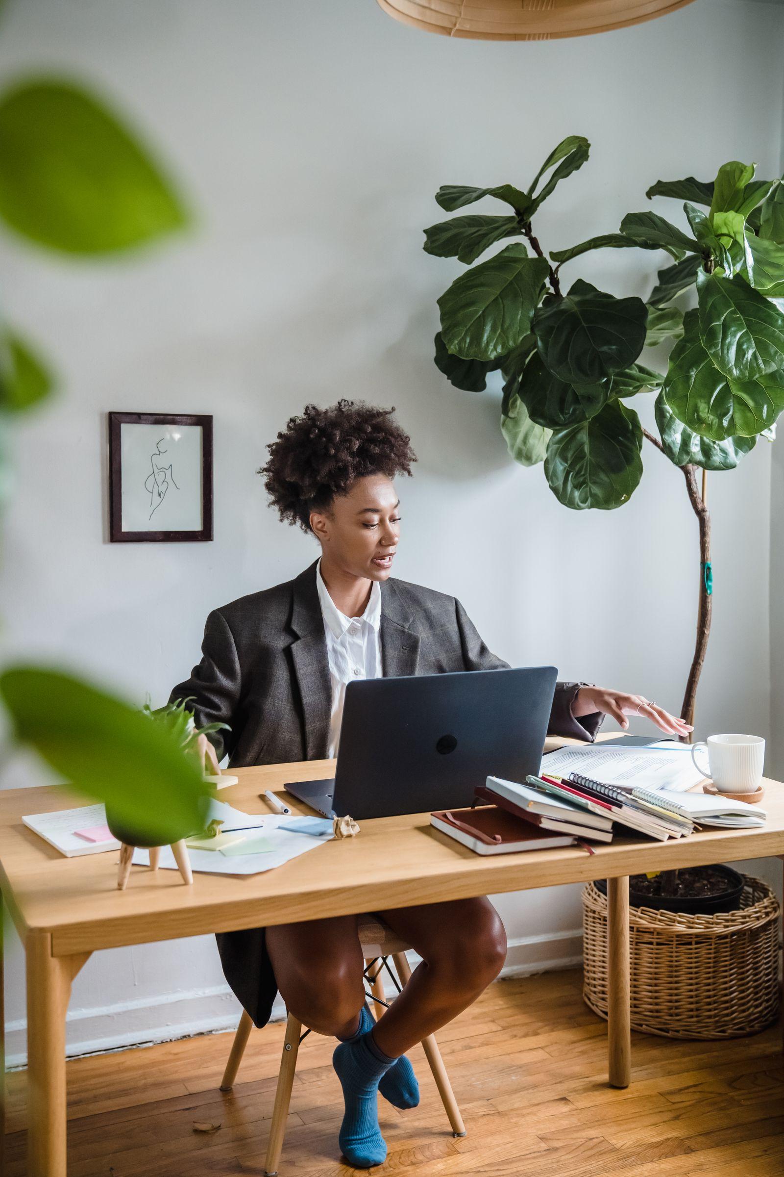 Femme en tenue professionnelle travaillant sur son ordinateur portable dans un bureau lumineux entouré de plantes