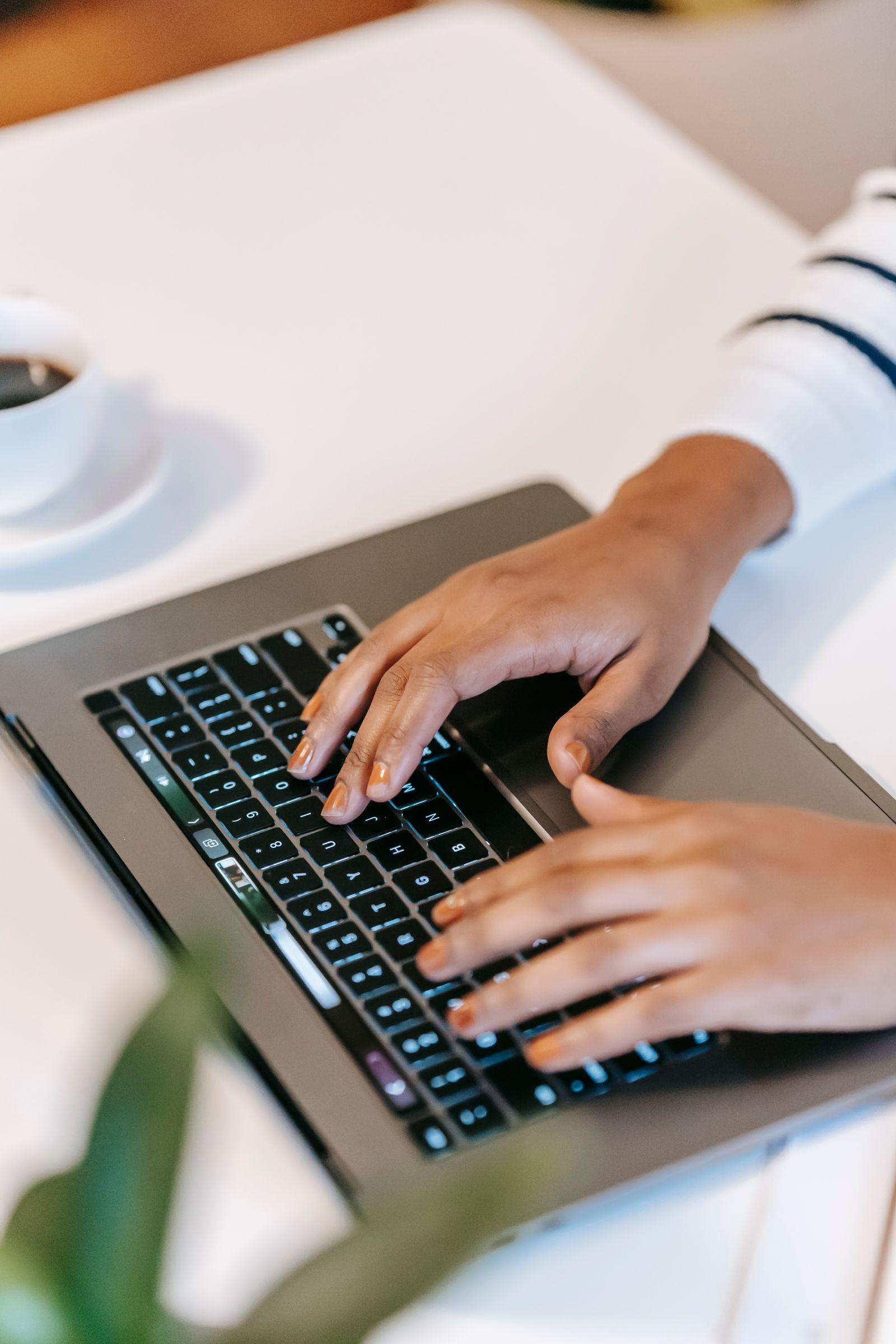 Mains sur un clavier d'ordinateur portable, tasse de café à proximité, pour illustrer le travail administratif à distance