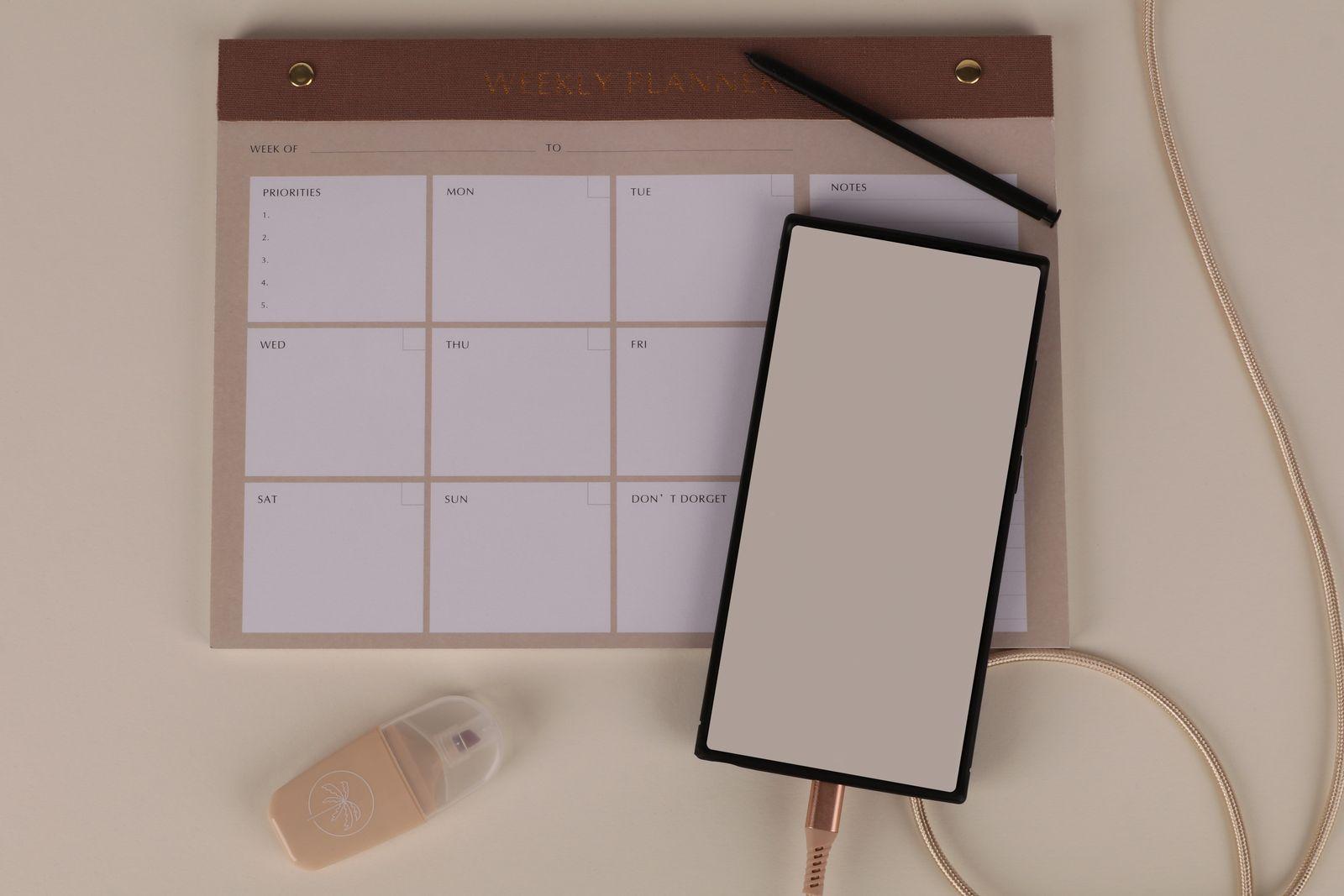 Planning hebdomadaire vierge posé sur un bureau avec un smartphone et un stylo