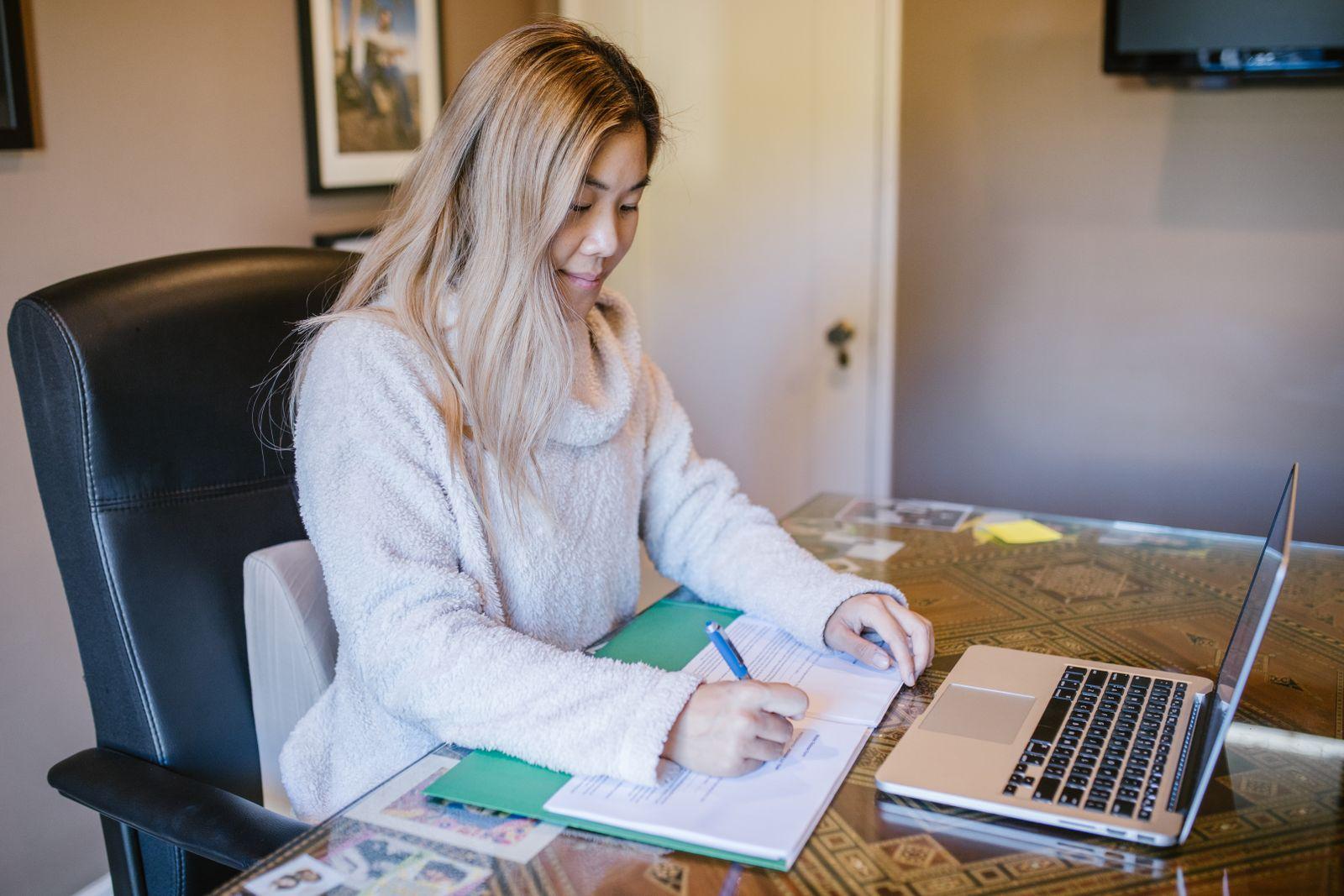 Femme signant un document à son bureau, ordinateur portable ouvert à côté