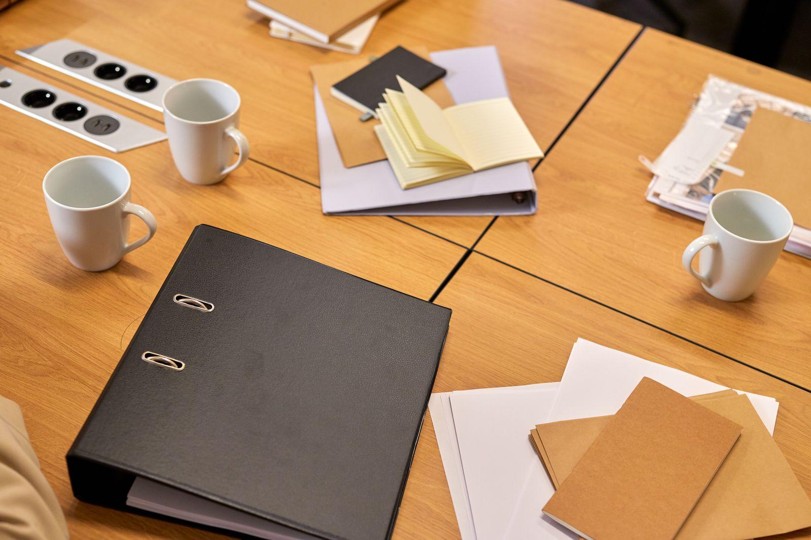 Classeur et documents administratifs posés sur une table de bureau avec des tasses de café
