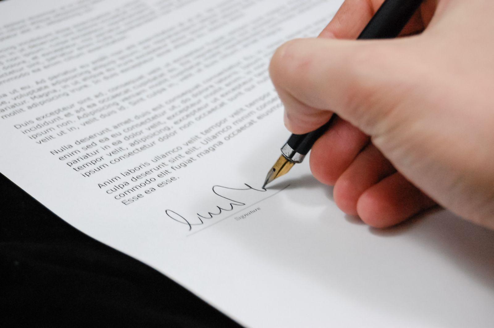 Main signant un document avec un stylo à plume, en gros plan