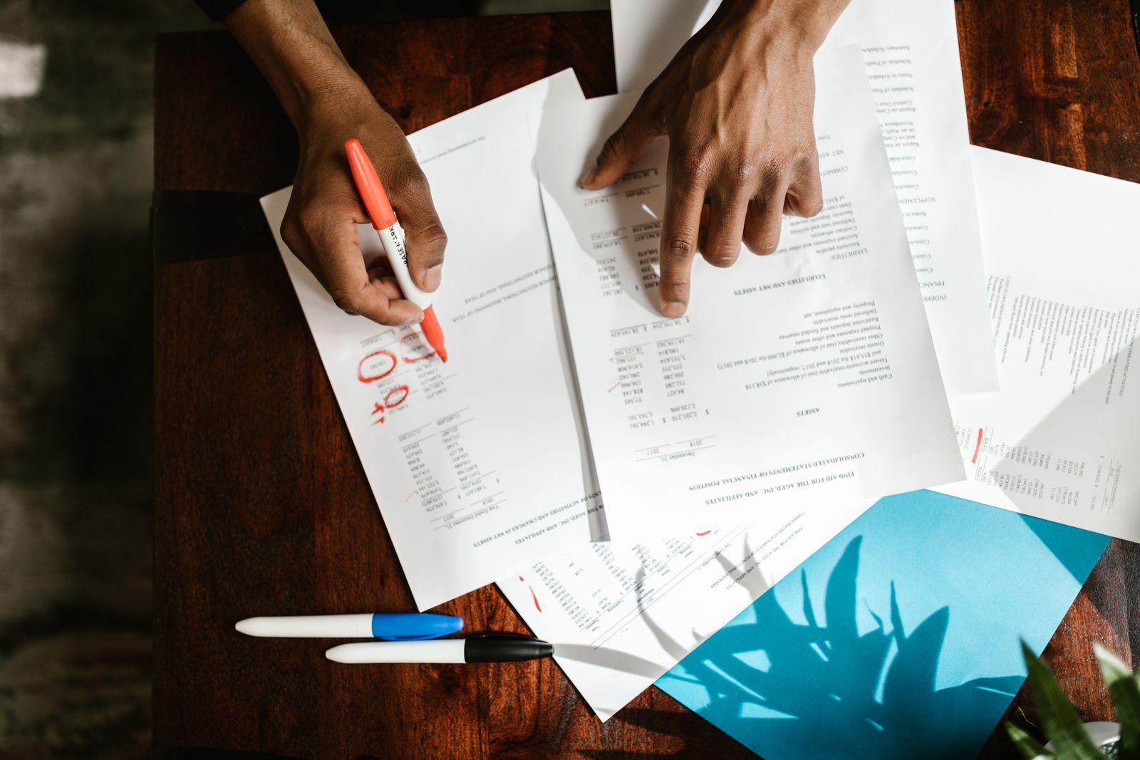 Mains annotant au feutre des documents financiers posés sur un bureau en bois
