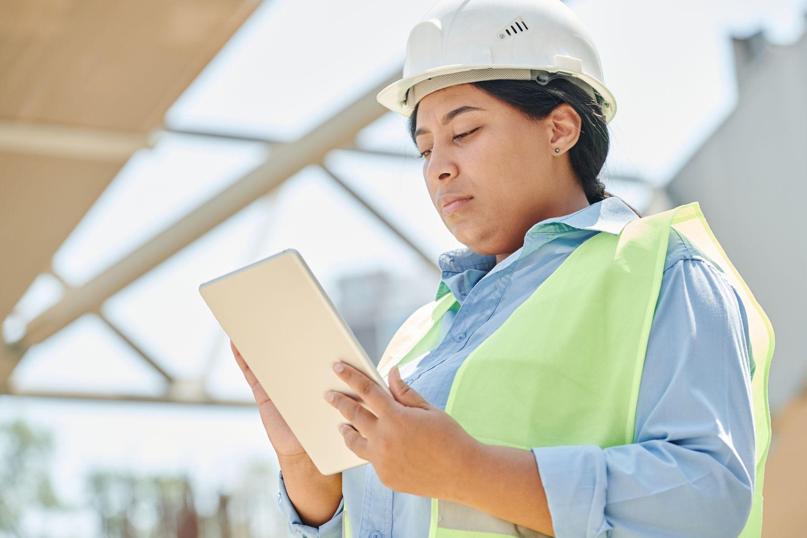 Ouvrière du bâtiment avec casque de chantier consultant une tablette numérique