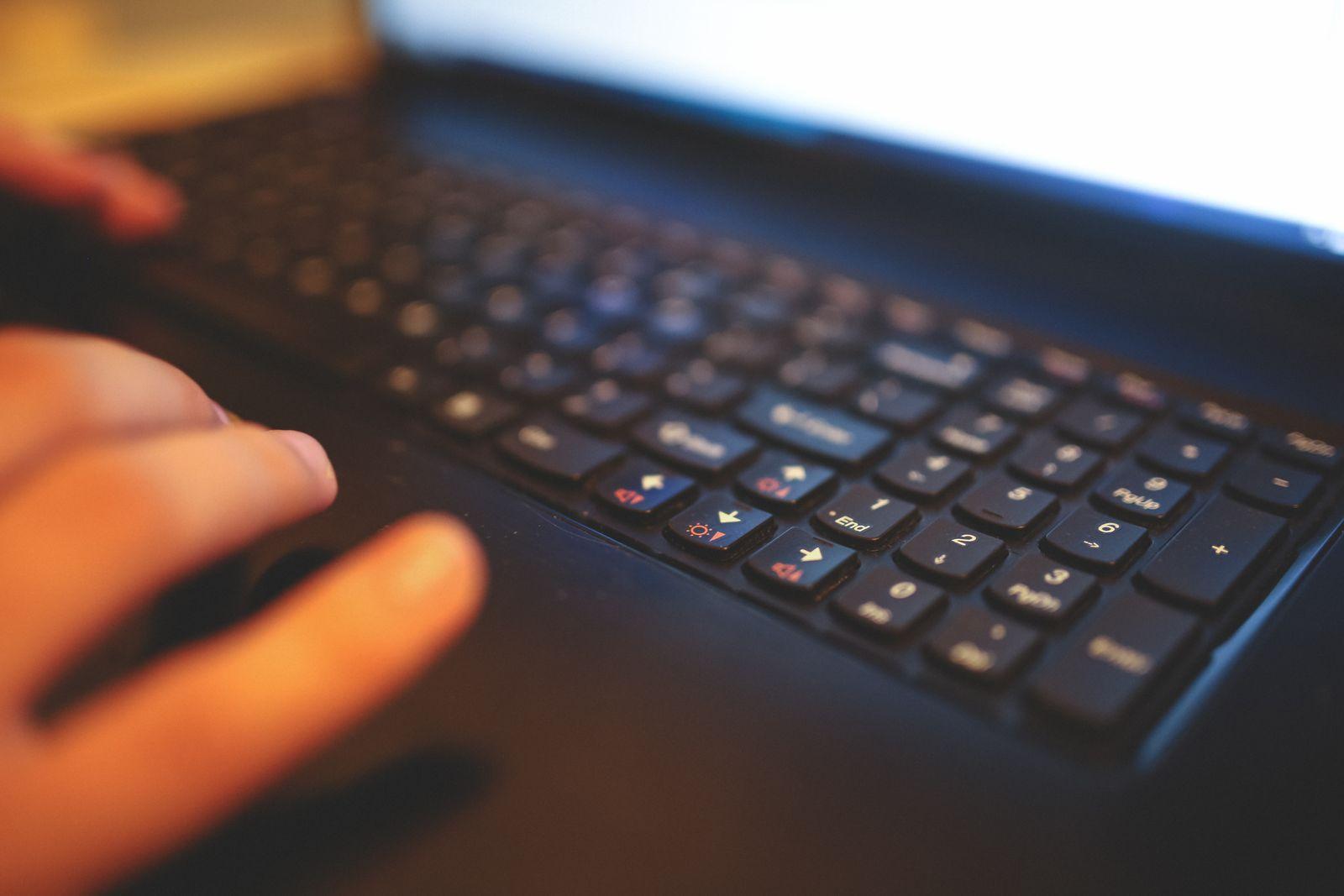 Gros plan sur des doigts tapant sur le clavier d'un ordinateur portable, avec l'écran lumineux en arrière-plan