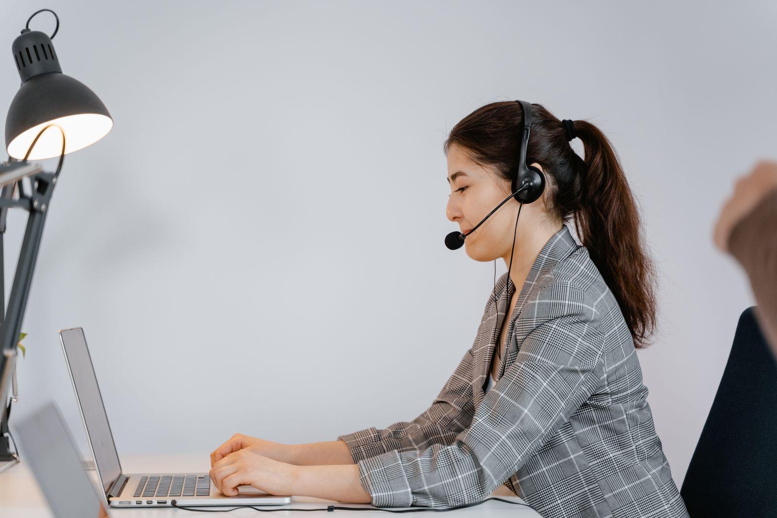 Femme portant un casque avec micro, assise devant un ordinateur portable dans un bureau lumineux