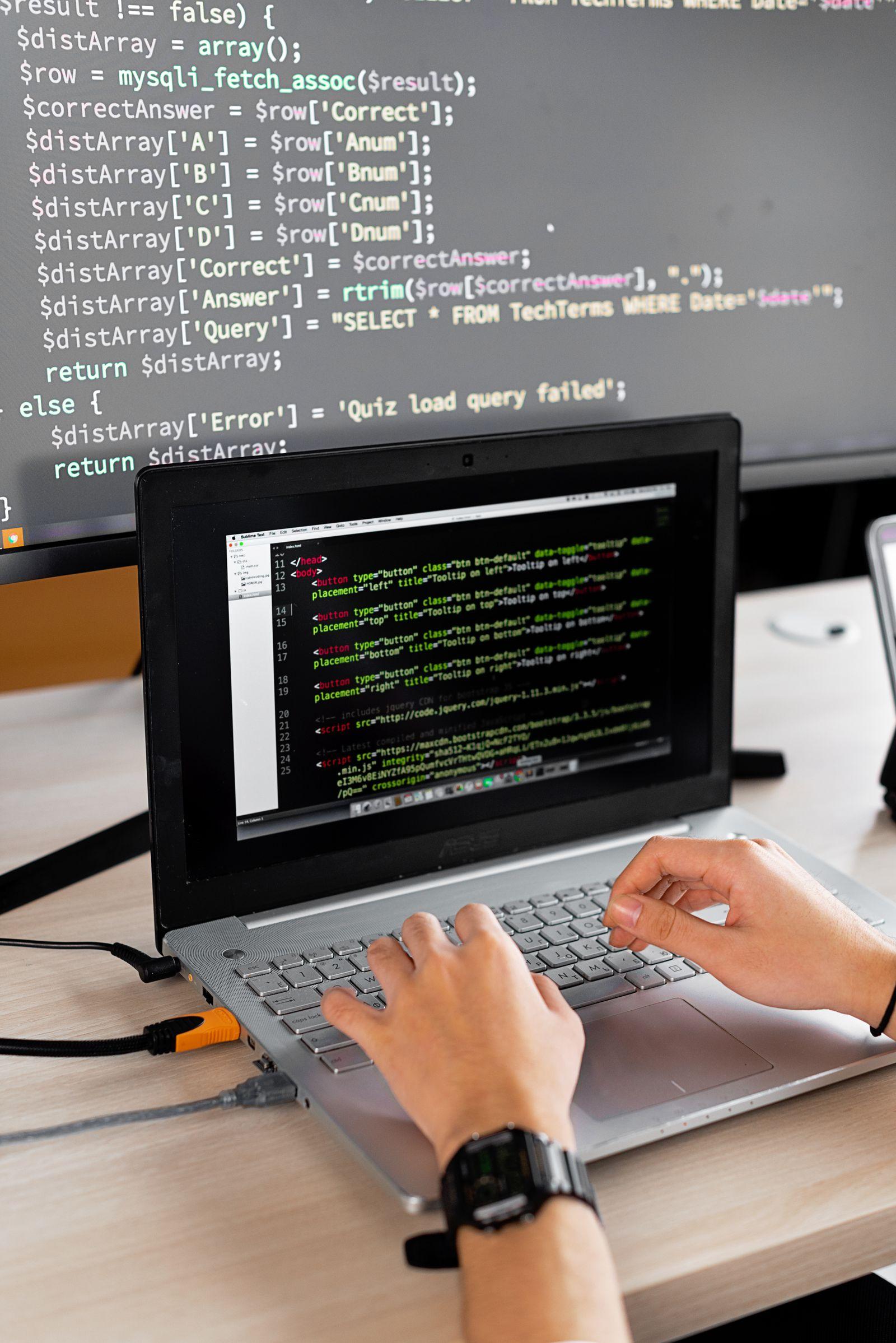 Développeur travaillant sur du code face à un écran d'ordinateur portable et un moniteur