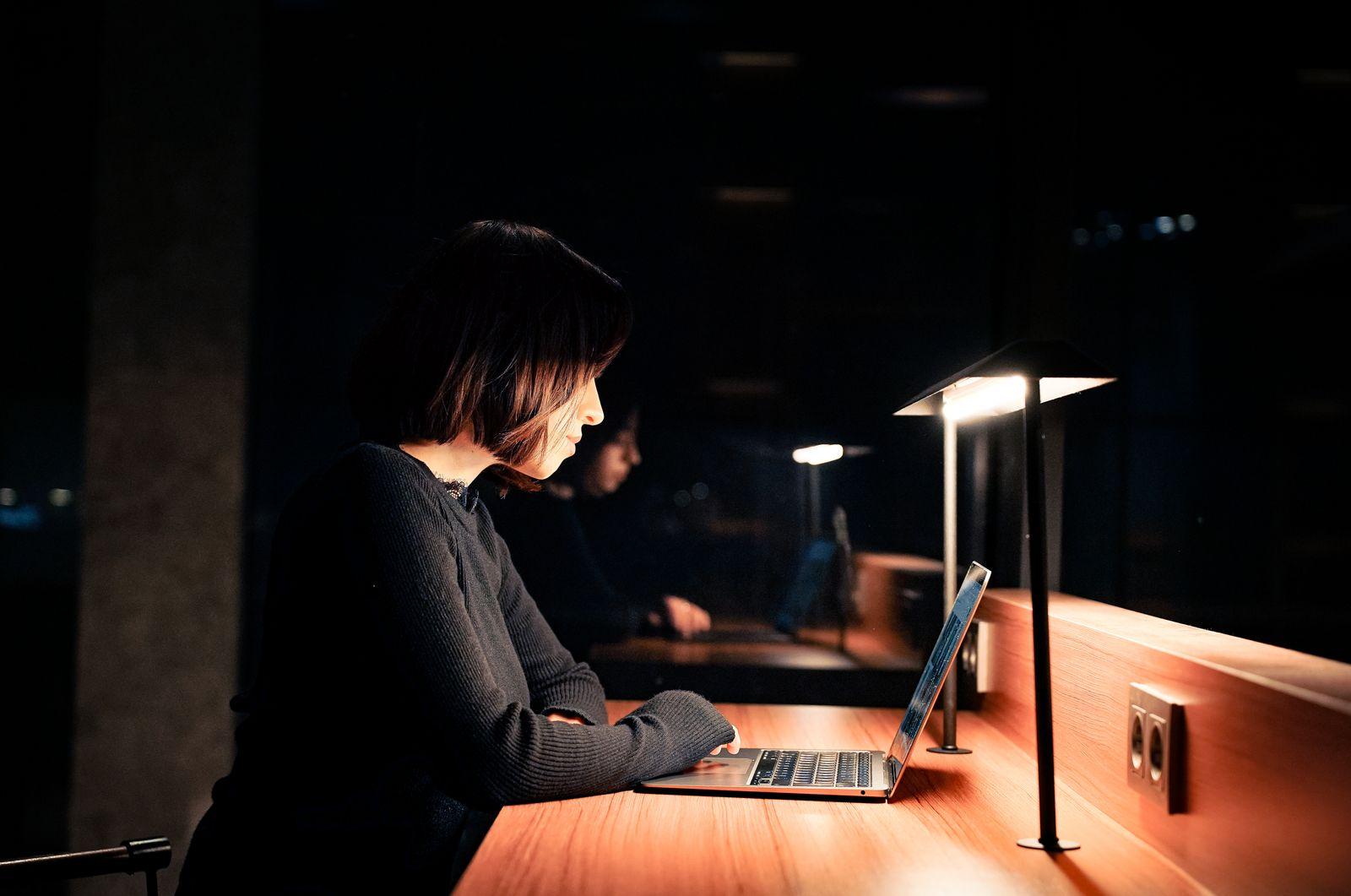 Femme travaillant tard le soir sur son ordinateur portable dans un bureau faiblement éclairé