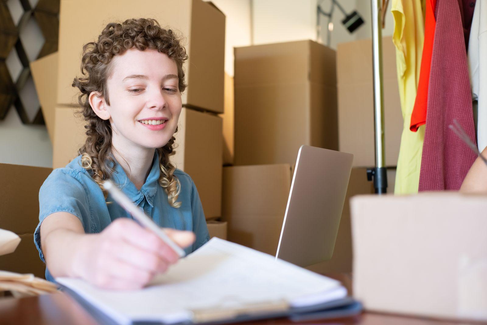 Une commerçante indépendante prend des notes dans son atelier entouré de cartons