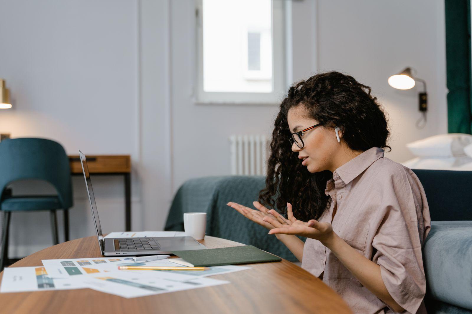 Femme en télétravail échangeant en visioconférence depuis son ordinateur portable, documents à portée de main