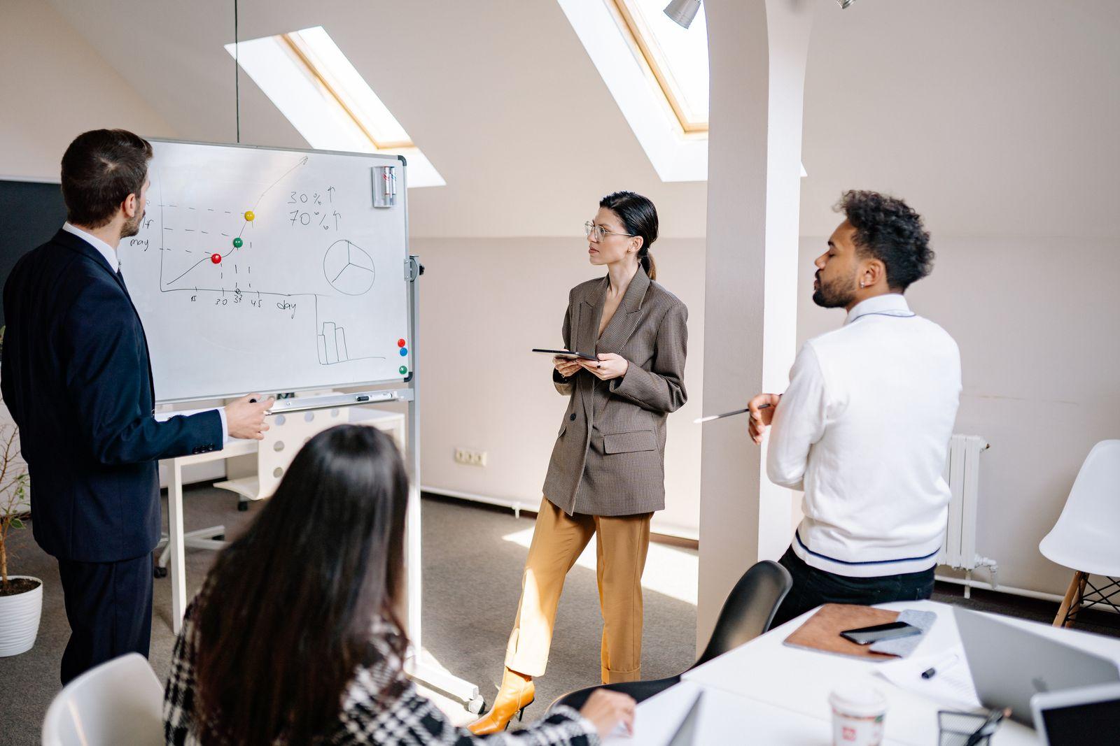 Équipe de professionnels échangeant devant un tableau blanc couvert de graphiques lors d'une réunion