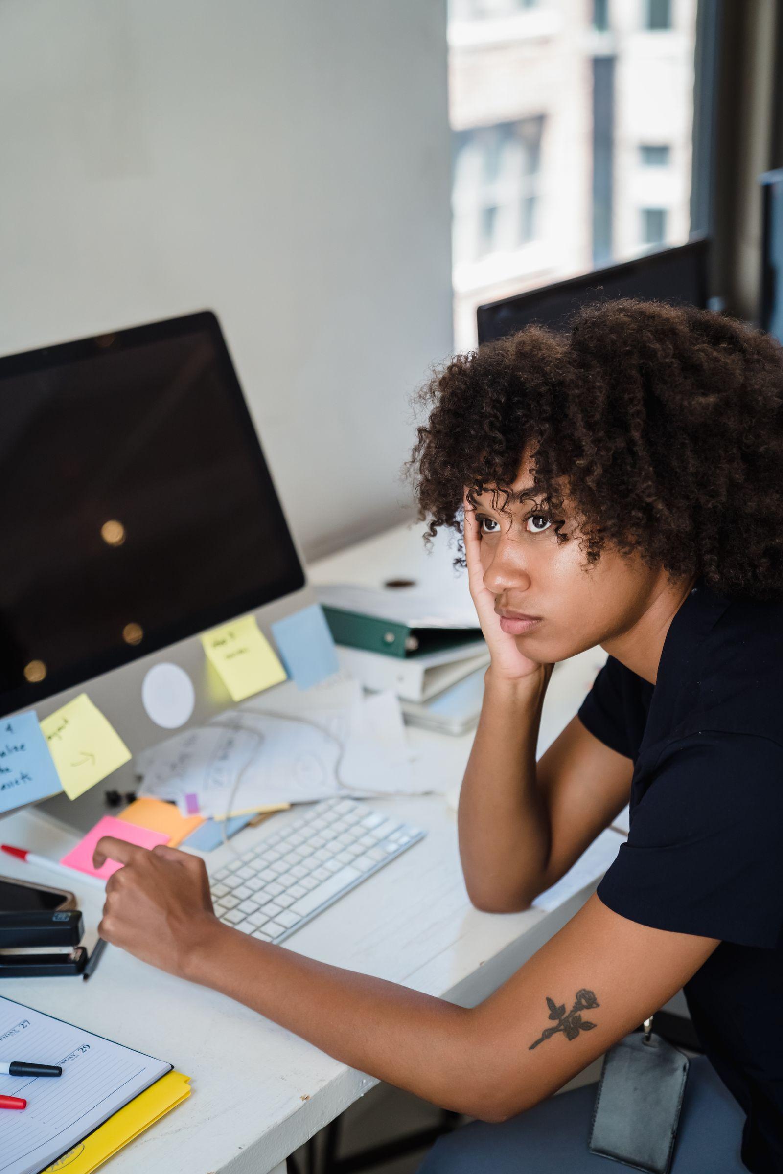 Femme pensive assise à son bureau, la tête posée sur la main, l'air préoccupé