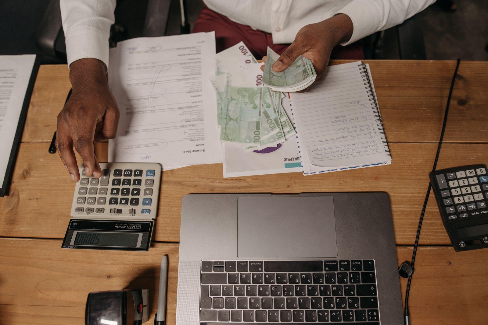 Un professionnel compte des billets et fait des calculs devant un bilan comptable