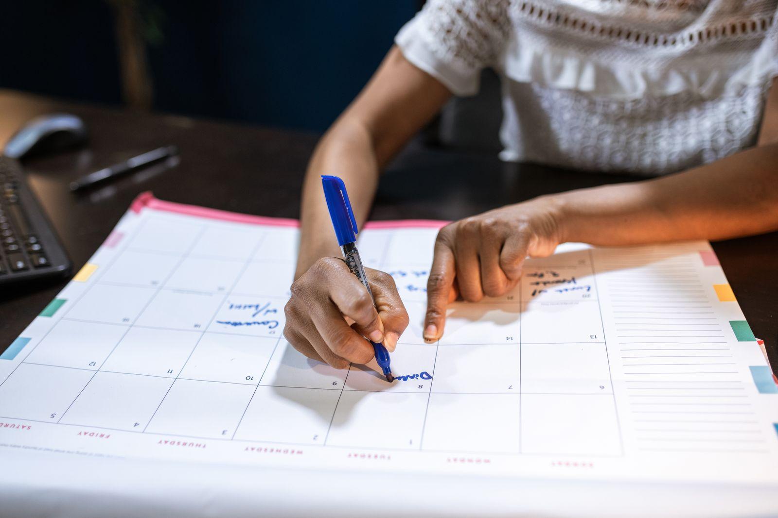 Une personne note un rendez-vous sur un planning hebdomadaire papier