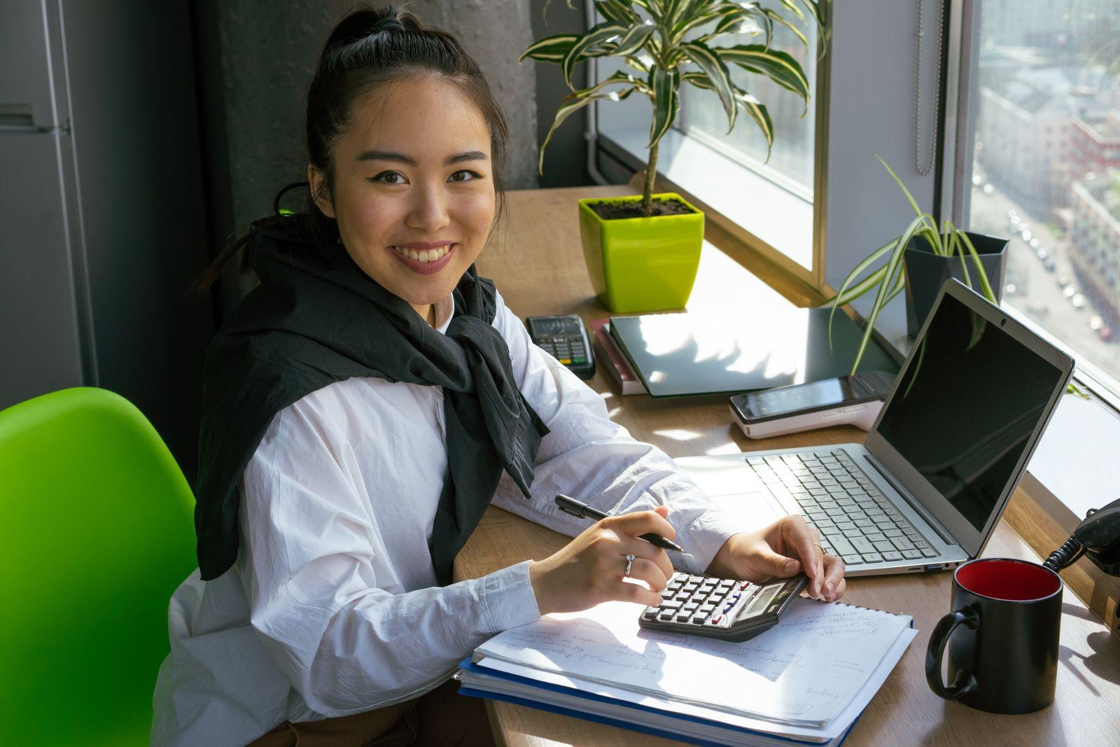 Une femme souriante utilise une calculatrice devant son ordinateur portable au bureau