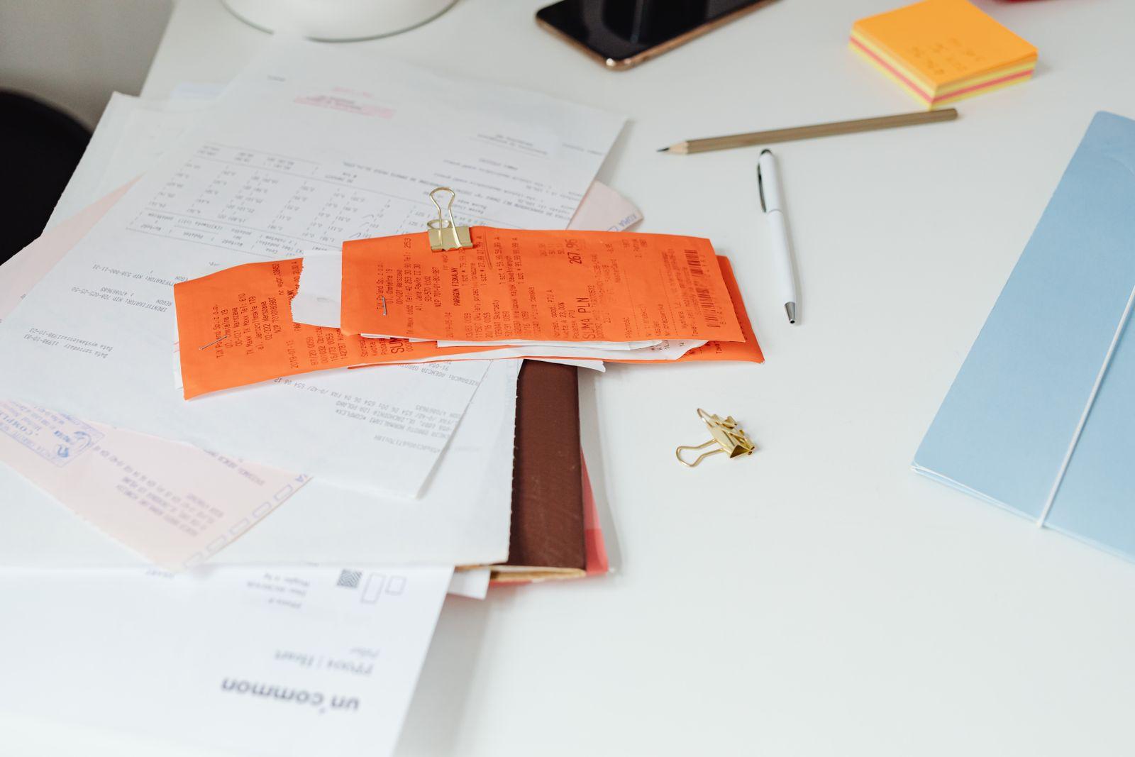 Factures et reçus papier empilés sur un bureau avec pince, stylo et blocs-notes