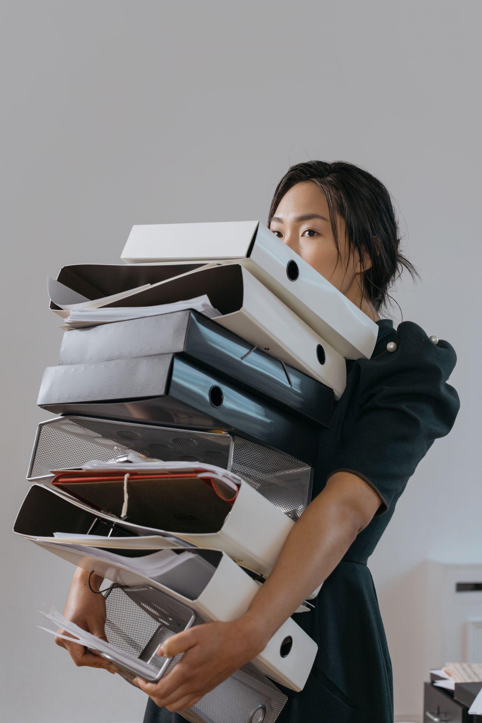 Femme portant une pile de classeurs et boîtes d'archives dans les bras