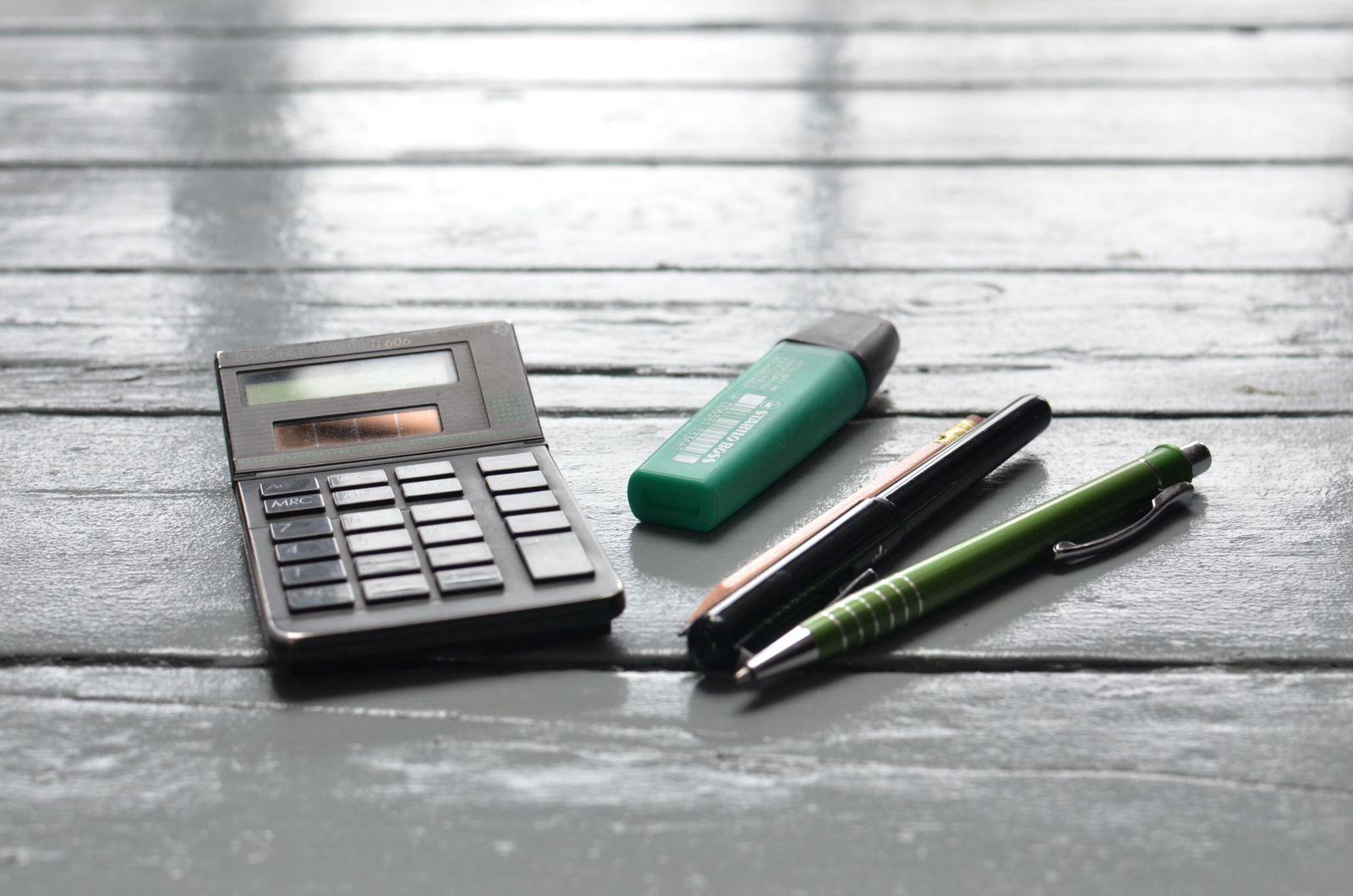 Calculatrice, surligneur et stylos posés sur une table en bois