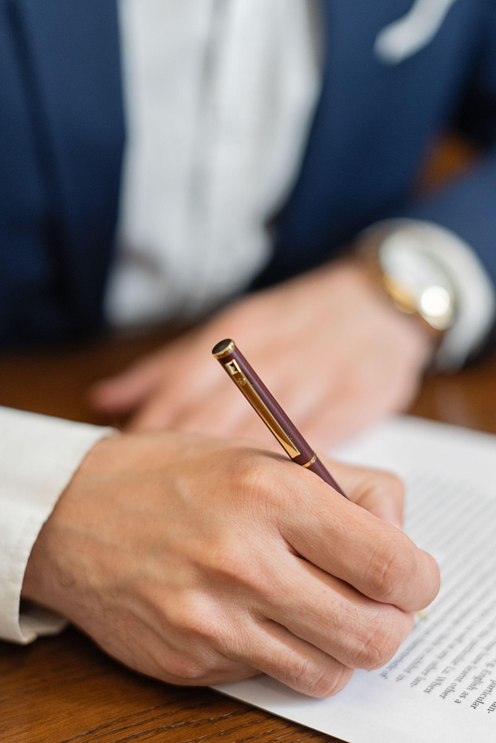 Gros plan sur une main signant un document avec un stylo, sur un bureau en bois