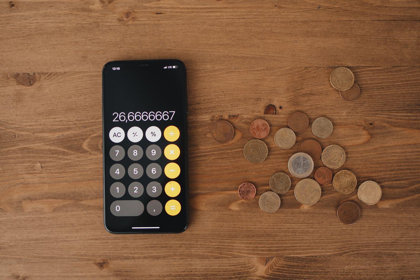 Smartphone affichant une calculatrice à côté d'un tas de pièces en euros sur une table en bois