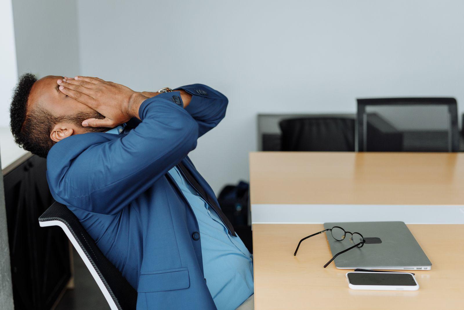 Dirigeant fatigué, tête en arrière et mains sur le visage, assis à son bureau